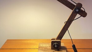 A desk lamp with a wooden base and a black shade, connected by a cord.