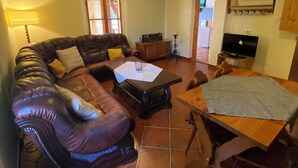 A living room with a leather sofa, a coffee table, a TV, and a dining table.