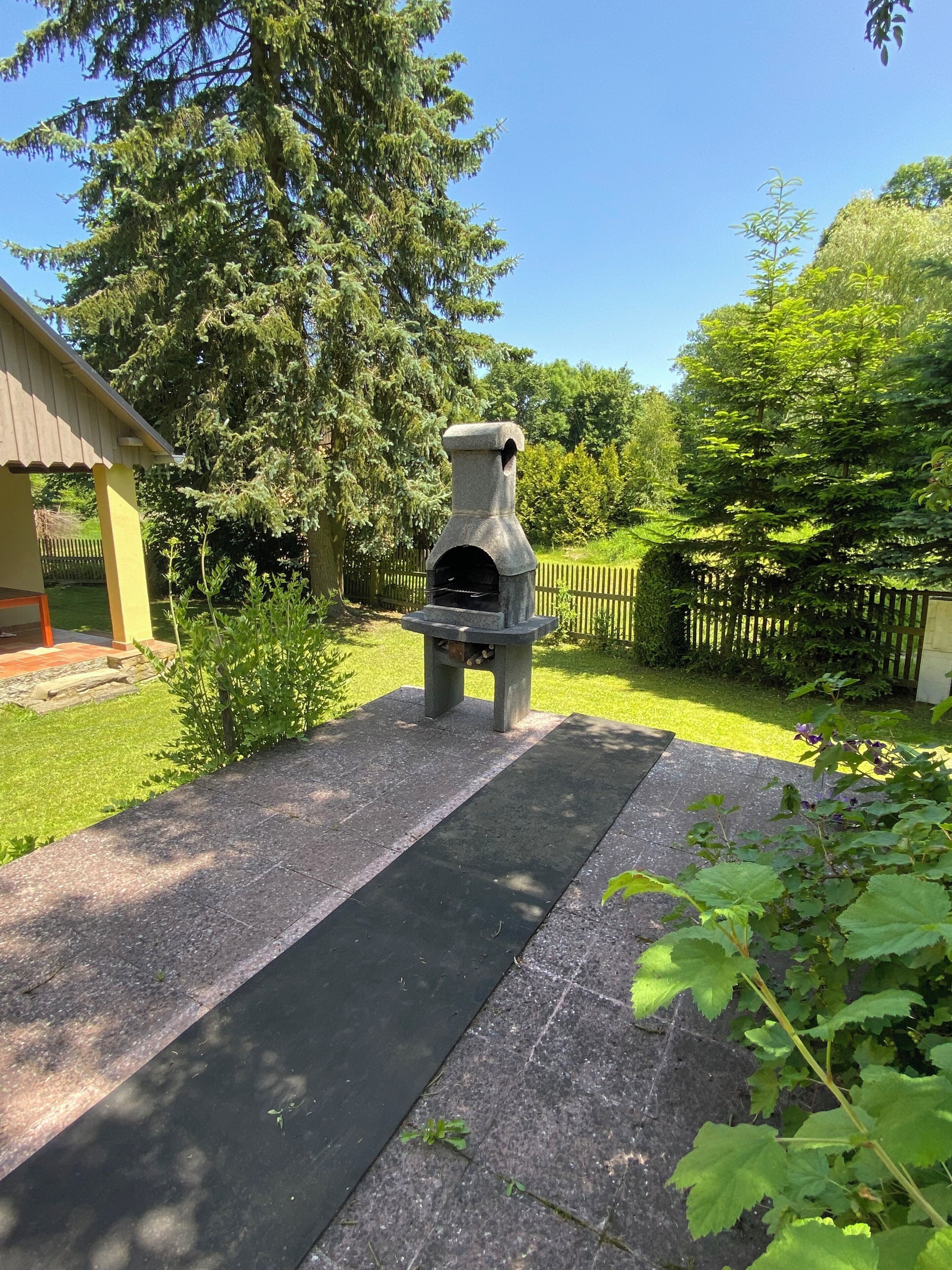 A stone outdoor oven in a yard with a wooden fence, grass, and trees.
