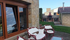 Ein Gebäude aus Stein mit roter Fassade, großen Fenstern und einer Terrasse mit Korbstühlen und einem kleinen Tisch.