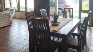 Ein Essbereich mit Holztisch und Stühlen, einer Topfpflanze und Blick auf ein geparktes Auto.