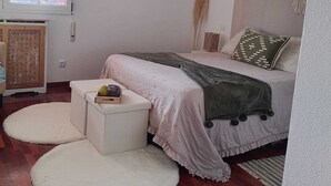 Ein Schlafzimmer mit einem Bett, einem kleinen weißen Tisch, zwei runden Wanddekorationen, einem Fenster und einem Rattanstuhl.
