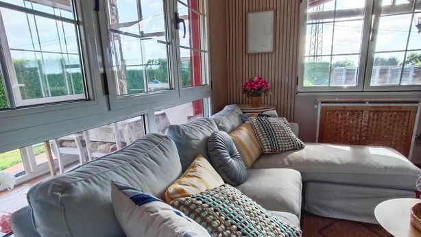 Ein modernes Wohnzimmer mit einem Ecksofa, einem kleinen runden Tisch und großen Fenstern.