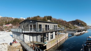 Una casa frente al agua con terraza, ventanas amplias y muelle.