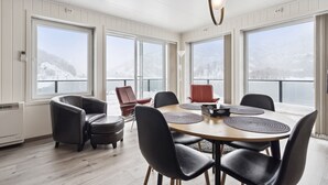 Un comedor con una mesa redonda, sillas negras y rojas, y ventanas amplias con vistas nevadas.