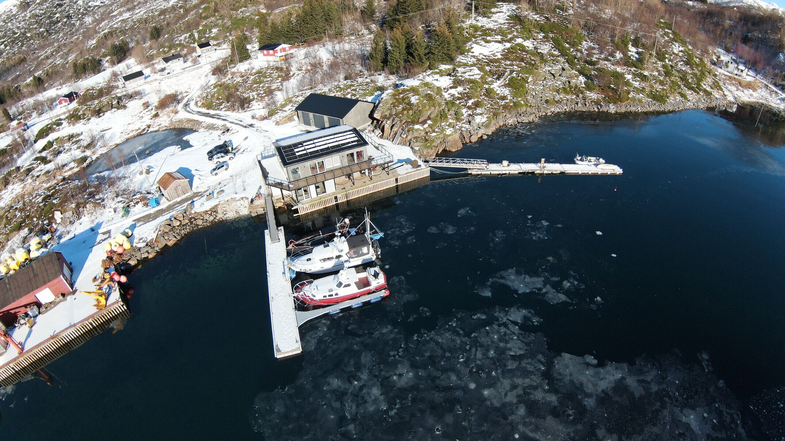 A pier extending into a lake with boats docked, surrounded by snow-covered terrain and buildings.