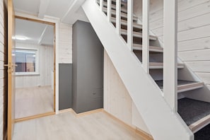 A staircase with wooden steps and white railings, leading to a room with a grey door and a window.
