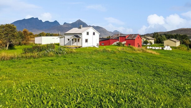 Un paisaje rural con una casa blanca, un granero rojo y montañas al fondo.