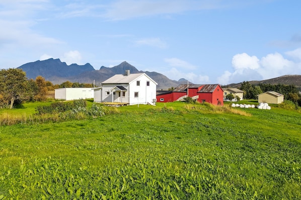 A rural landscape with a white house, red barn, and mountains in the background.