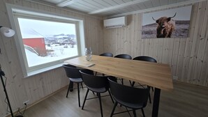 Un comedor con una mesa de madera, sillas negras, un ventanal con vista a un edificio rojo y un cuadro de un toro en la pared.