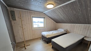 Una habitación con dos camas, una ventana, una escalera de madera y una mesita.
