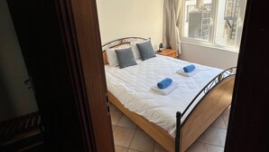 Ein Schlafzimmer mit einem Bett, einem Nachttisch, einem Fenster mit Vorhängen und Blick nach draußen.