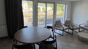 Ein Zimmer mit einem runden Tisch, zwei Stühlen, einem Sofa und Blick auf ein Gebäude durch große Fenster.