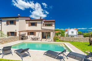 A two-story house with a swimming pool, outdoor seating, and a stone wall.