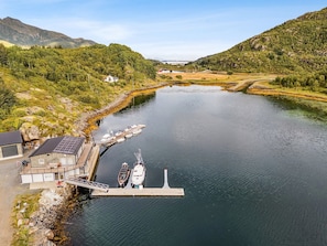 Ein Fluss mit an einem Steg vertäuten Booten, umgeben von Grün und Bergen.