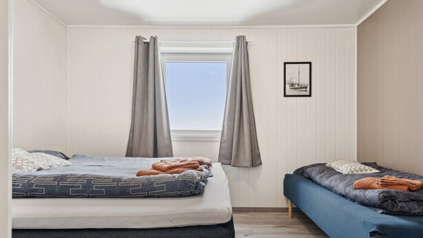 A room with a bed, a sofa, a window with curtains, and a framed picture on the wall. - Valen Brygge, Digermulen (Vågan)