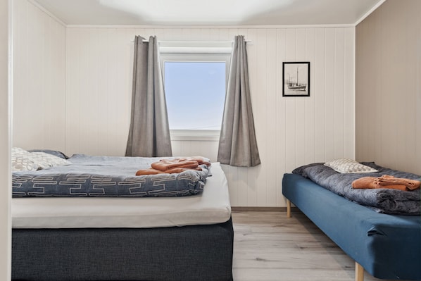 Ein Zimmer mit einem Bett, einem Sofa, einem Fenster mit Vorhängen und einem gerahmten Bild an der Wand.