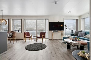 Una sala de estar moderna con televisión, asientos y ventanas amplias.