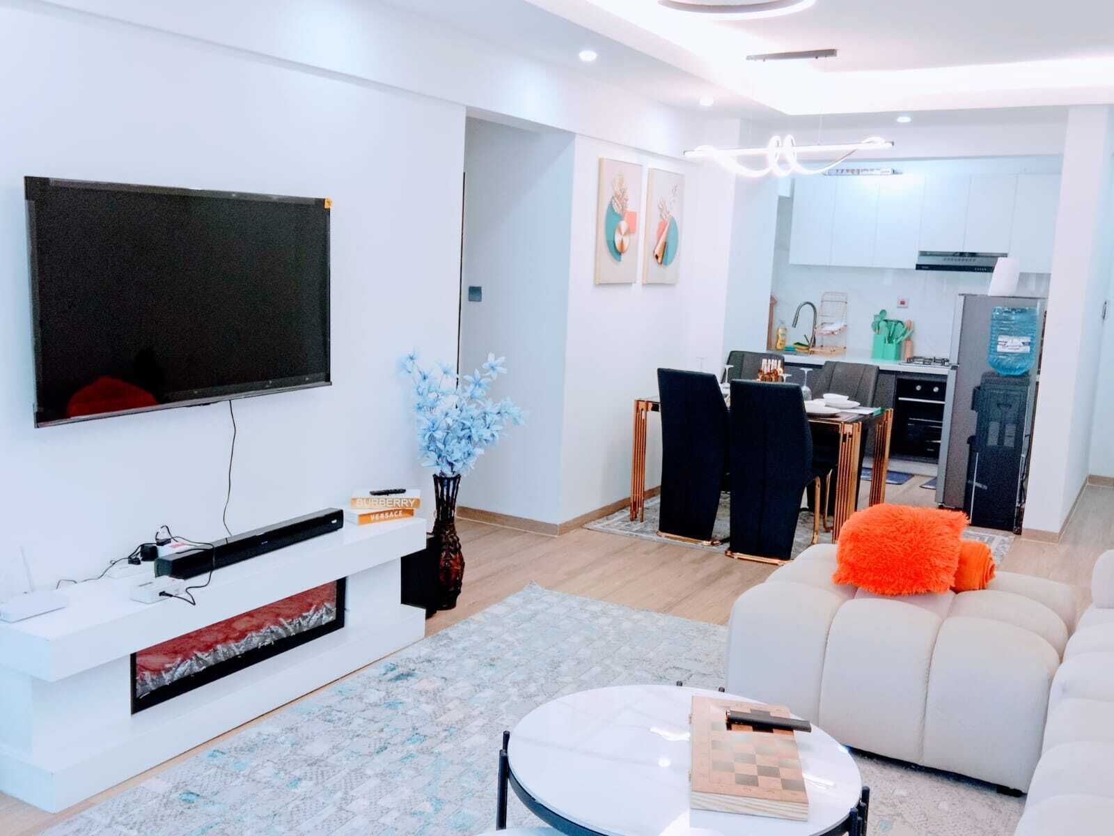 Una sala de estar moderna con televisor de pantalla plana, chimenea, comedor y cocina.