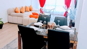 A modern living room with a sofa, dining table, chairs, and a large window with red curtains. - Marina Bay View Palace Apartment (Nairobi)