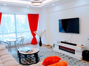 Ein modernes Wohnzimmer mit einer Couch, einem runden Couchtisch, einem an der Wand montierten Fernseher und einem Fenster mit roten Vorhängen.
