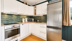 Een moderne keuken met witte kasten, een roestvrijstalen koelkast, een magnetron, een koffiezetapparaat en een inbouwoven.