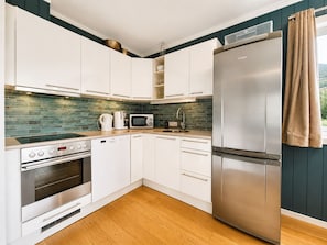 Una cocina moderna con armarios blancos, un refrigerador de acero inoxidable, un microondas, una cafetera y un horno empotrado.