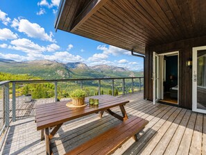 A wooden deck with a picnic table, a basket, and a view of mountains.