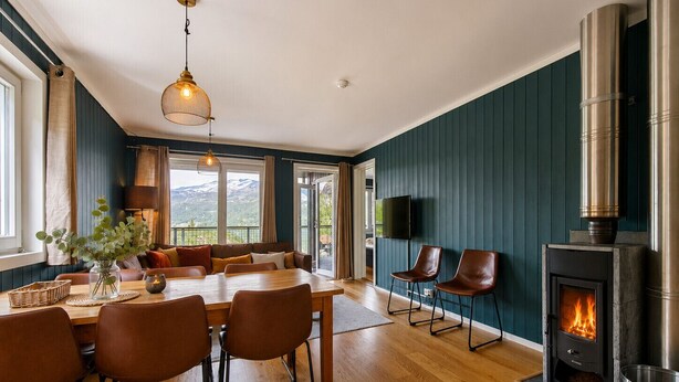Een moderne woonkamer met een open haard, houten vloeren, een eettafel met stoelen, een bank en een groot raam met uitzicht.