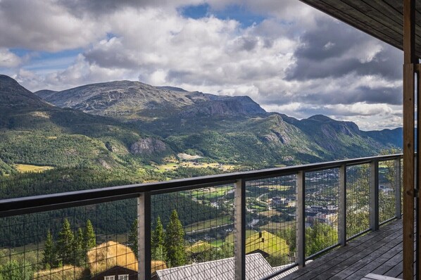 A balcony with a metal railing overlooking a mountainous landscape with a town below.