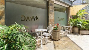 Een glazen deur met 'DAWN' aanduiding, buitenzitplaatsen met metalen stoelen en potplanten.