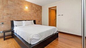 Een slaapkamer met een bed, een nachtkastje, een wandlamp en een houten vloer.