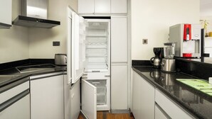 Een keuken met een inbouwkoelkast, een fornuis, een koffiezetapparaat en een blender.