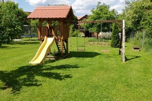 Eine hölzerne Spielanlage mit Rutsche und Schaukeln auf einer Rasenfläche.