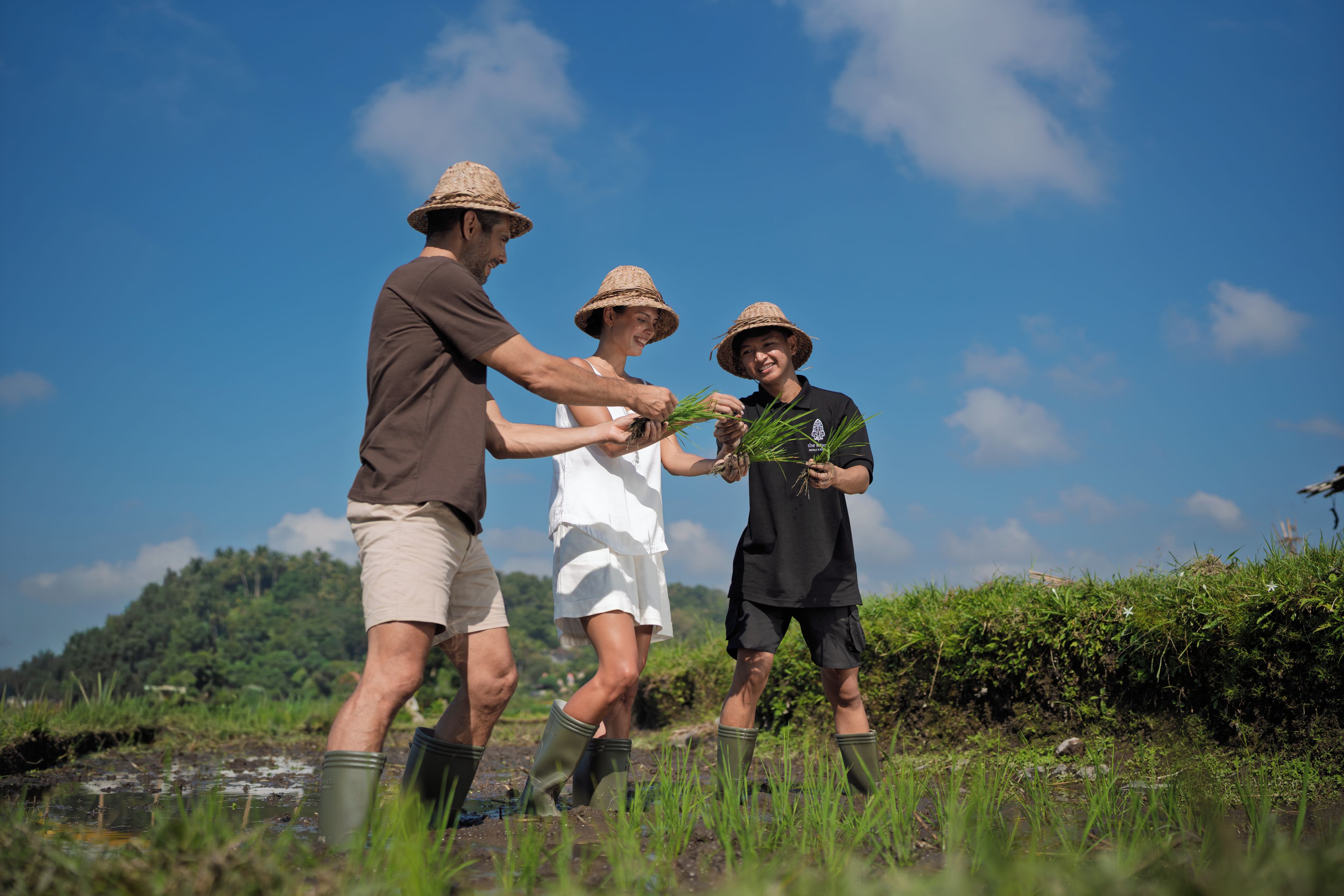 Three people in a natural setting with a clear sky, wearing casual clothing and hats.