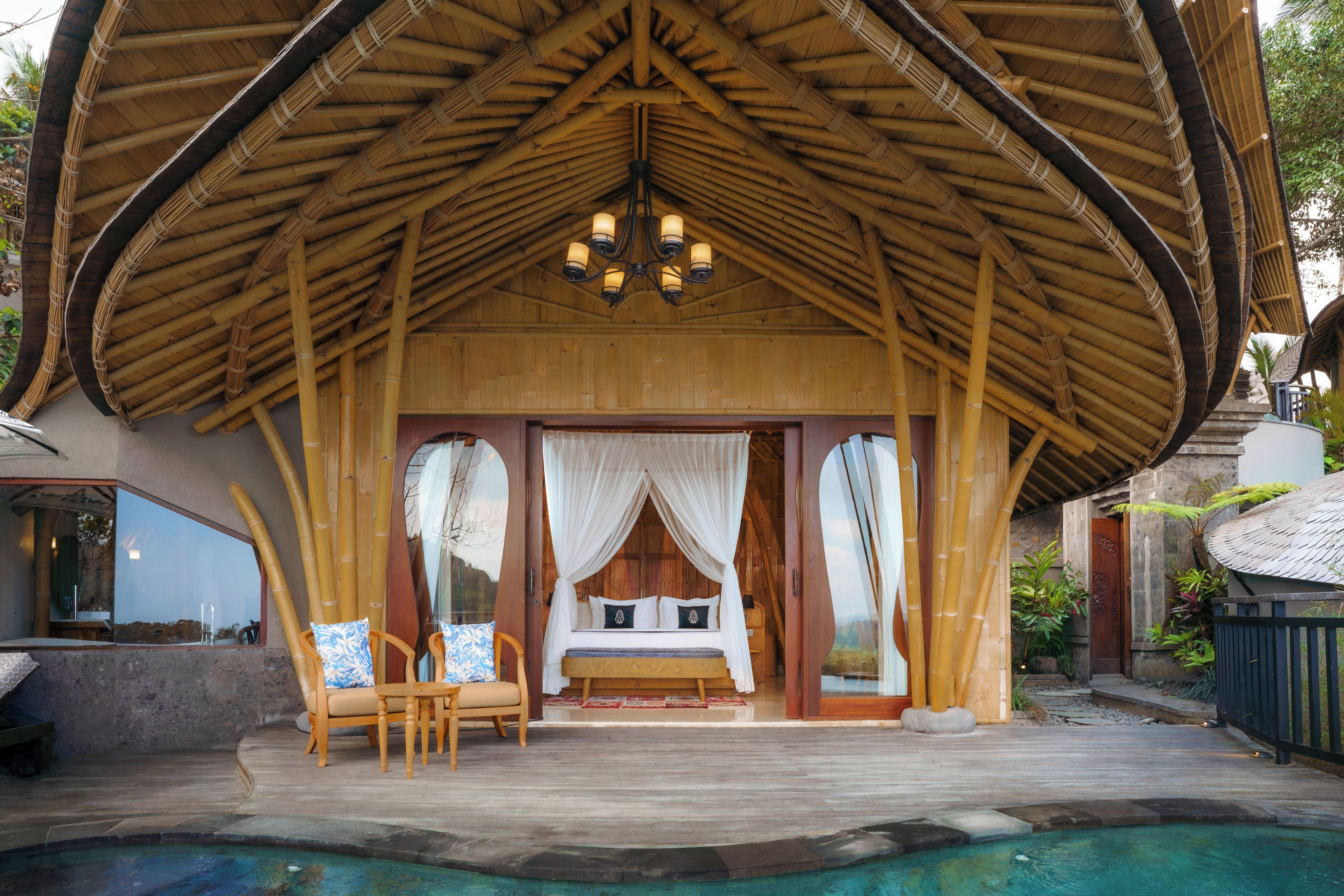 Un bungalow avec un toit de chaume, une piscine et un lit agrémenté de rideaux blancs.