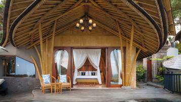 Un bungalow avec un toit de chaume, une piscine et un lit agrémenté de rideaux blancs.
