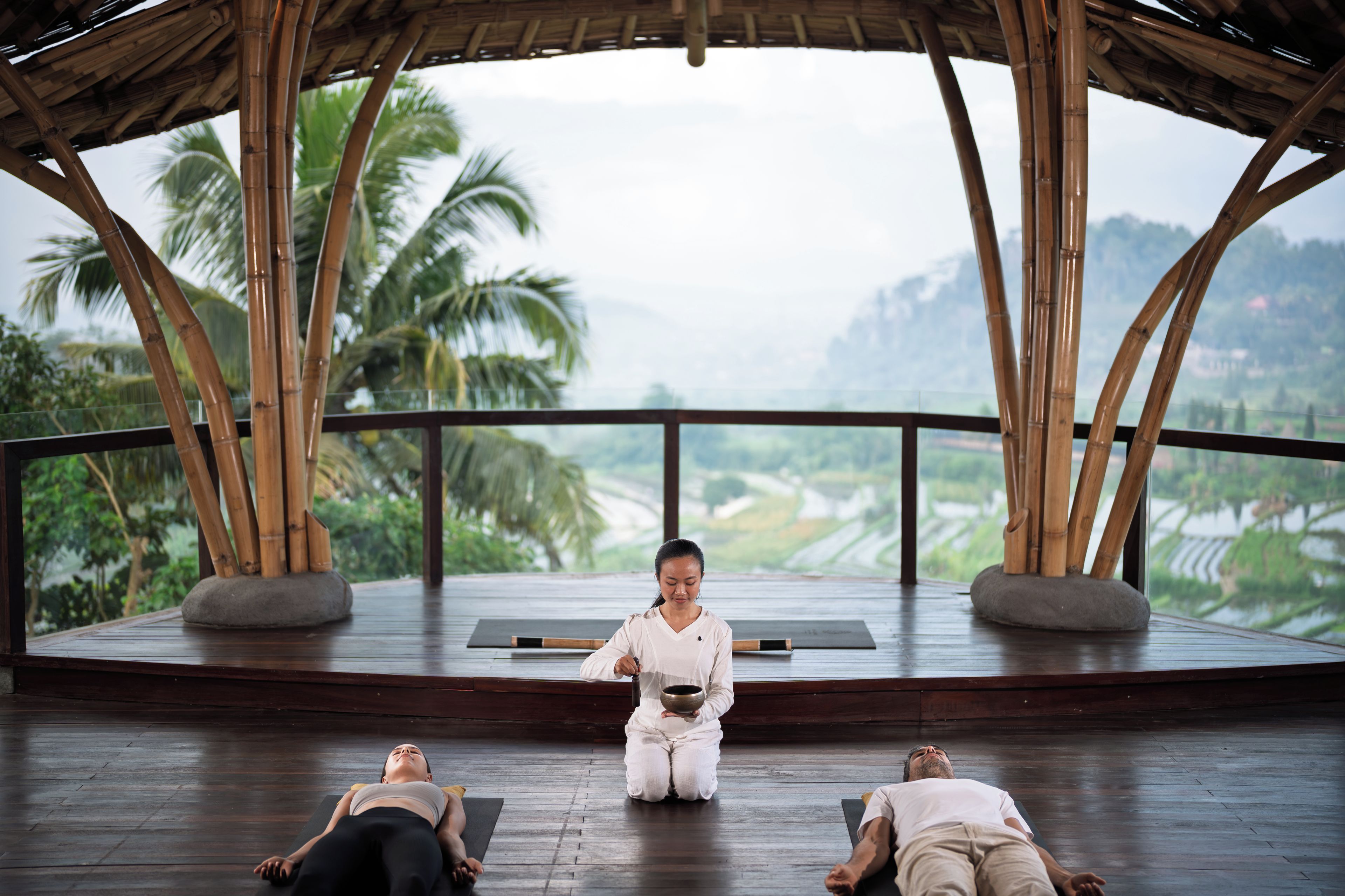 Clase de yoga en un pabellón de madera con vistas a palmeras y un paisaje montañoso.