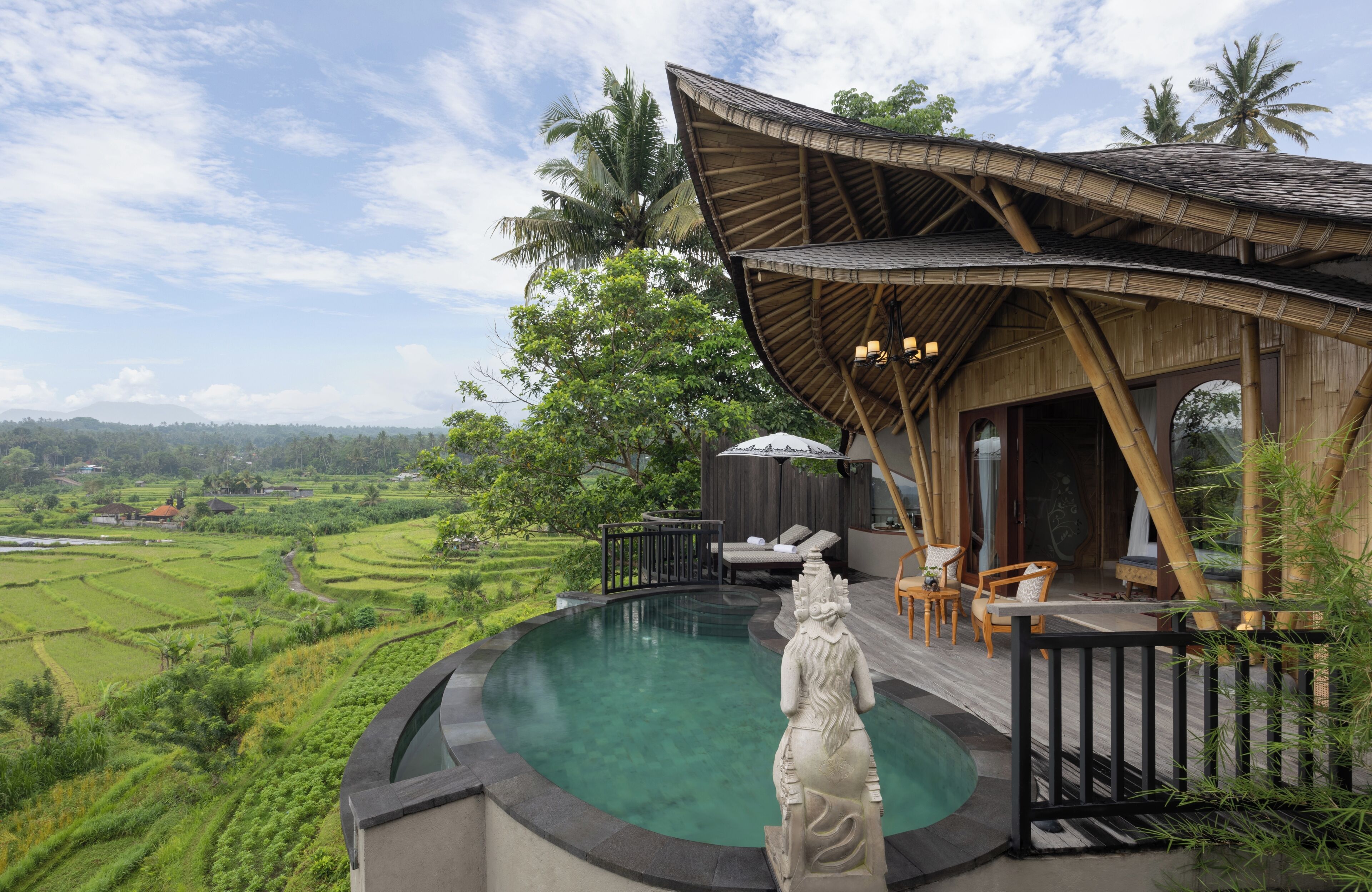 A pool with a statue, a wooden structure with a curved roof, and a view of green fields.