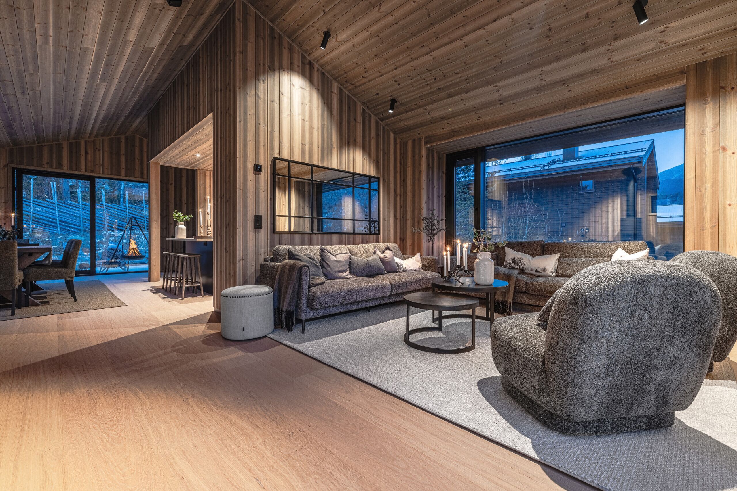 A spacious living area with a wooden ceiling, large windows, a sofa, a coffee table, and a stone armchair.