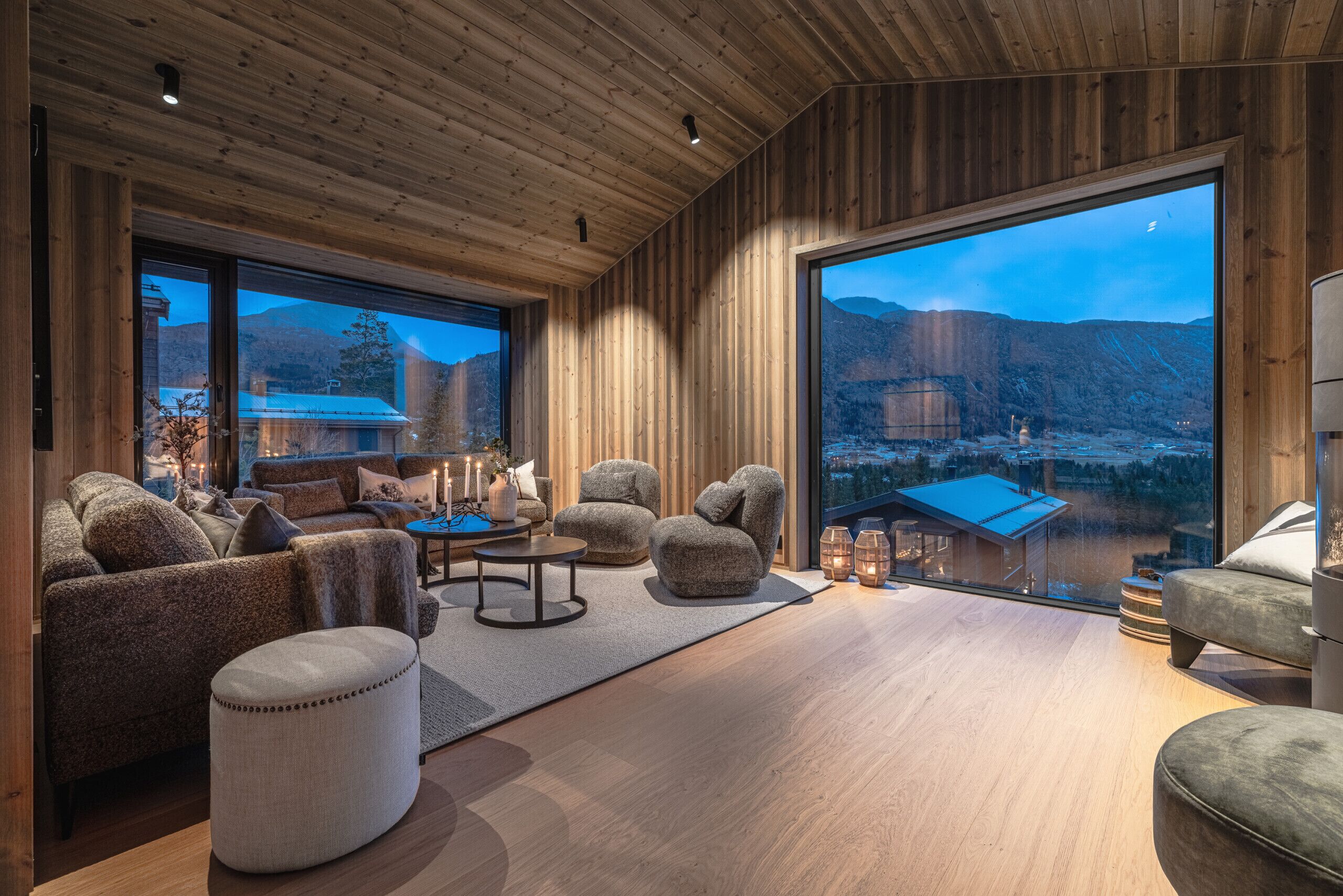Un salon moderne aux murs en bois et aux grandes fenêtres, comprenant un canapé, des fauteuils et une table basse.