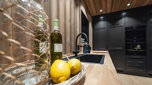 Una cucina con piano di lavoro in legno, lavello e pensili. In un cesto, due bottiglie d'olio d'oliva e due limoni.