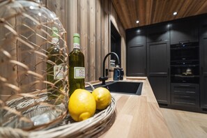 Una cocina con encimera de madera, un lavamanos y armarios. Hay dos botellas de aceite de oliva y dos limones en una cesta.