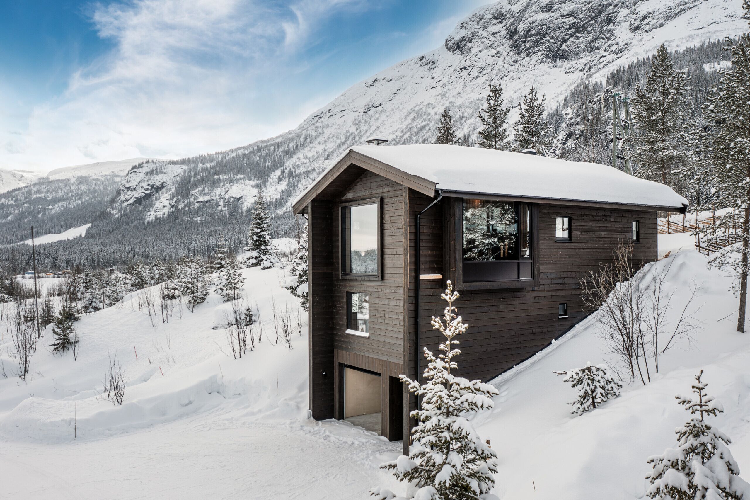 A wooden cabin with a large window, situated on a snowy mountain slope.