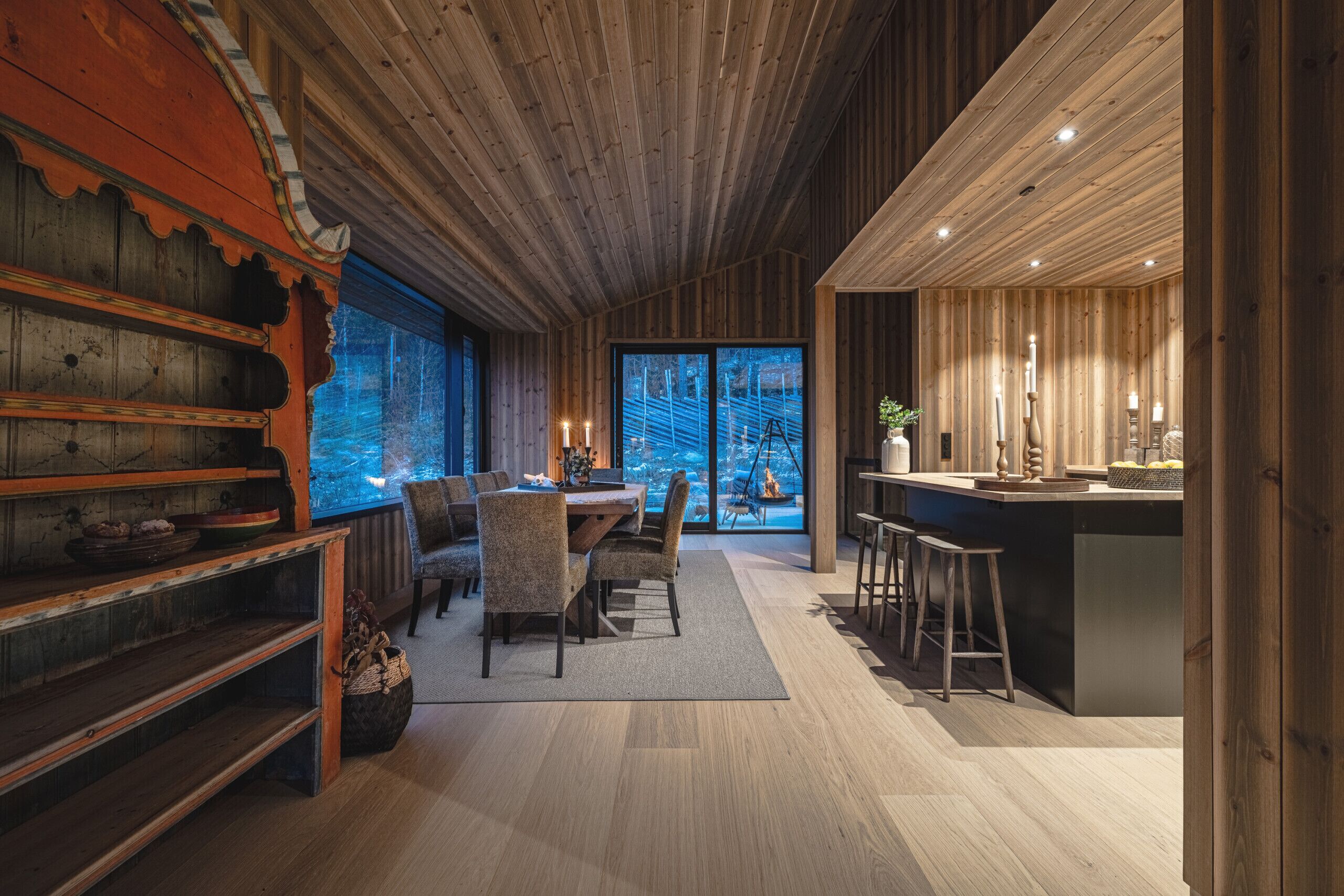 A modern interior with wooden paneling, a dining area with chairs and a table, and a kitchen with stools.