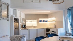 Een moderne keuken met witte kastjes, een inbouwoven en een eethoek met een ronde tafel en blauwe stoelen.