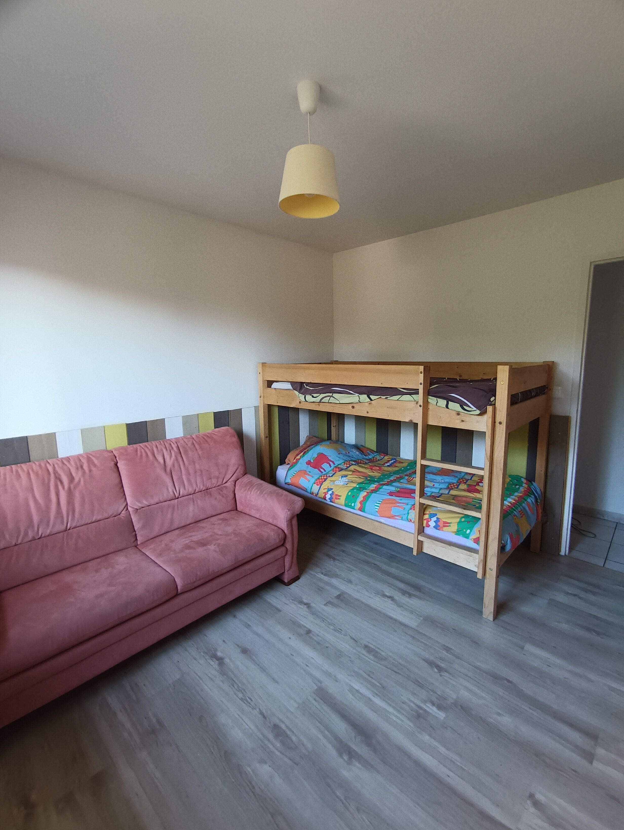 Une pièce avec un lit superposé, un canapé rose et un luminaire suspendu.