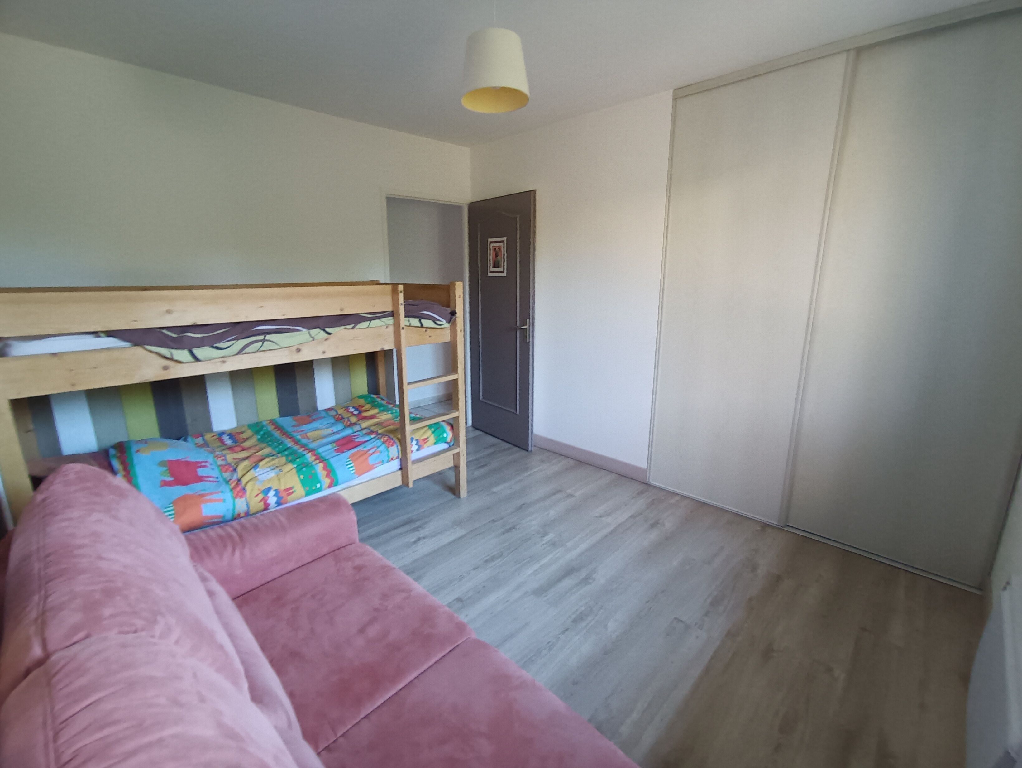 A room with a bunk bed, a wardrobe, a door, and a light fixture.