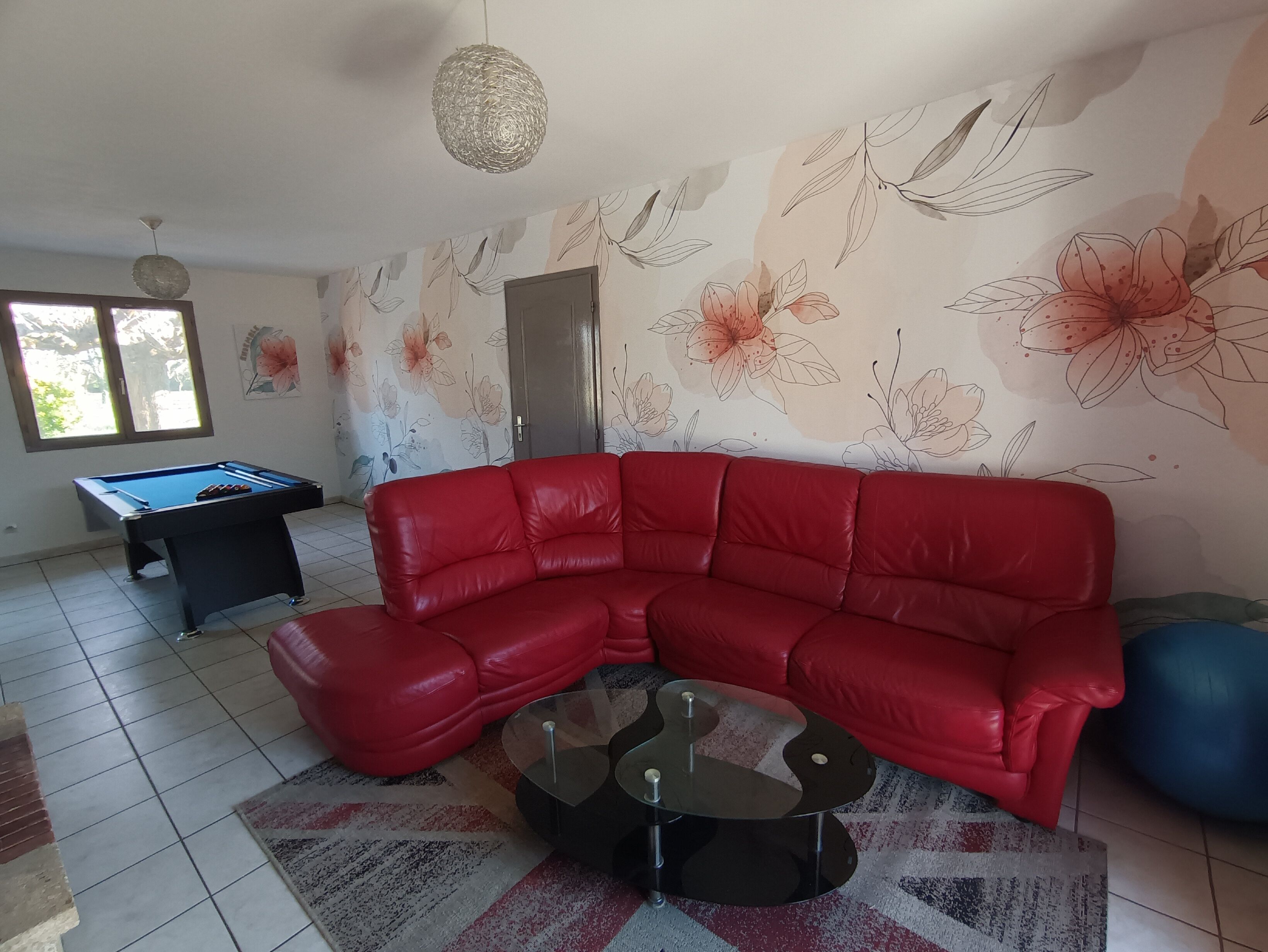 A living room with a red sofa, a pool table, a decorative wall, and a ceiling light fixture.