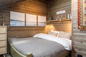 Camera da letto in una baita di legno, con un letto, opere d'arte a parete, uno scaffale con libri e un tappeto decorativo.